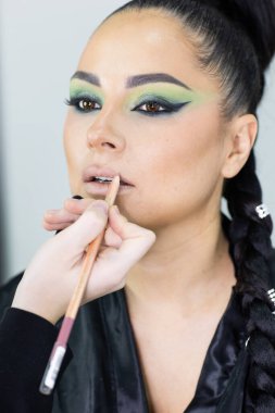 Beautiful European woman getting artistic makeup applied by a professional makeup artist in a modern beauty salon, glamour and elegance concept.