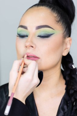 Modern bir güzellik salonu, cazibe ve zarafet konseptinde profesyonel bir makyöz tarafından sanatsal makyaj yaptıran güzel Avrupalı bir kadın..