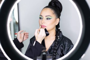 Beautiful European woman getting artistic makeup applied by a professional makeup artist in a modern beauty salon, glamour and elegance concept.