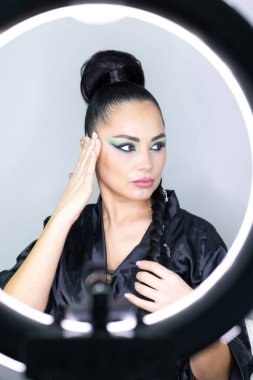 Beautiful European woman getting artistic makeup applied by a professional makeup artist in a modern beauty salon, glamour and elegance concept.