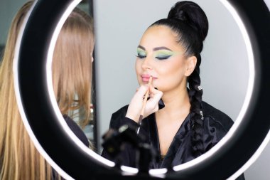 Beautiful European woman getting artistic makeup applied by a professional makeup artist in a modern beauty salon, glamour and elegance concept.