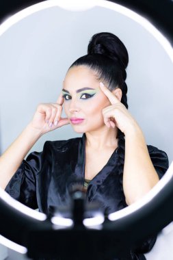 Beautiful European woman getting artistic makeup applied by a professional makeup artist in a modern beauty salon, glamour and elegance concept.