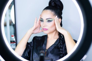 Beautiful European woman getting artistic makeup applied by a professional makeup artist in a modern beauty salon, glamour and elegance concept.