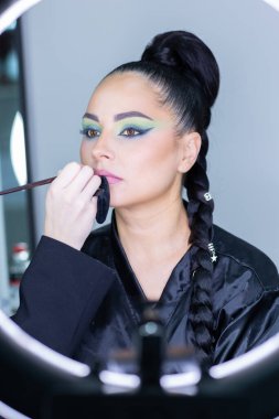 Beautiful European woman getting artistic makeup applied by a professional makeup artist in a modern beauty salon, glamour and elegance concept.