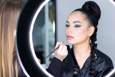 Beautiful European woman getting artistic makeup applied by a professional makeup artist in a modern beauty salon, glamour and elegance concept.