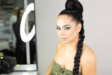 Beautiful European woman getting artistic makeup applied by a professional makeup artist in a modern beauty salon, glamour and elegance concept.