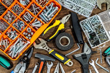 Ahşap bir arka planda düzenlenmiş ev yapımı ve onarım aletleri. Cilt, pense, civata, çekiç, makas, elektrik bandı ve DIY projeleri, ev geliştirme, yenileme, bakım ve atölye kavramları için gerekli el aletlerini içerir.