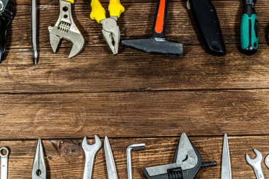 Ahşap bir arka planda düzenlenmiş ev yapımı ve onarım aletleri. Cilt, pense, civata, çekiç, makas, elektrik bandı ve DIY projeleri, ev geliştirme, yenileme, bakım ve atölye kavramları için gerekli el aletlerini içerir.