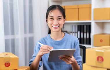 Küçük işletmeler kurmak, dijital tablette çalışan genç Asyalı kadınlar ve müşterilere kutu teslimat ürünlerini işaretlemek, internetten sipariş etmek.