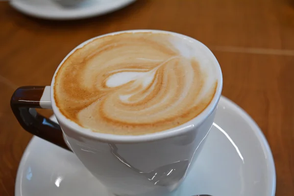 Delicioso capuchino espumoso en una taza blanca en un plato — Foto de Stock