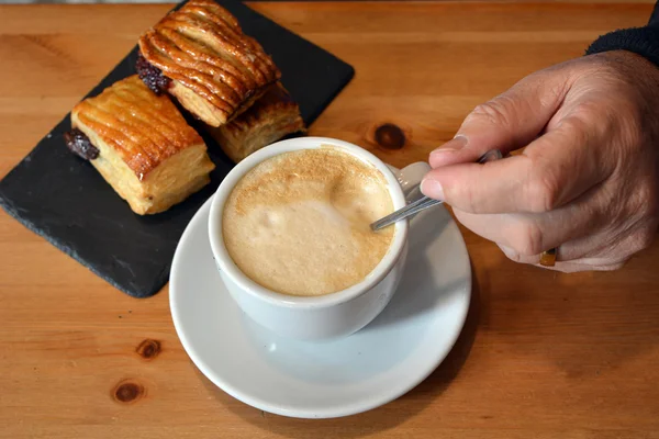 Man's  hand stirring a hot cappuccino on the wooden table — Stock Photo, Image