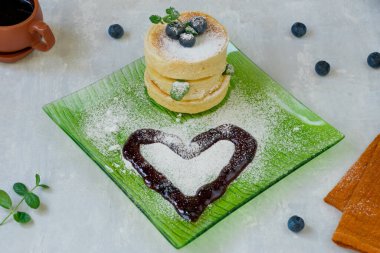 Kare yeşil tabakta üzerine krema serpiştirilmiş yaban mersini serpiştirilmiş Japon krepleri. Hafif arkaplan. Kalp reçelden yapılmış. Lezzetli kahvaltı..