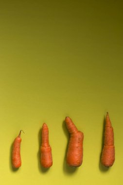 Çirkin yemek. Zeytin rengi arka planda deforme olmuş organik havuçlar. Yiyecek atığı konsepti. Minimalizm, pop sanatı. Dikey pozisyonda. Boşluğu kopyala.