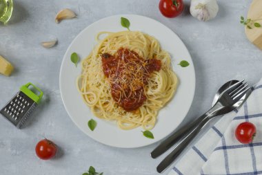 Geleneksel İtalyan spagettisi bolonez beyaz yuvarlak tabakta ve hafif arka planda. Makarna için malzemeler - kirazlı domates, parmesan, sarımsak, zeytinyağı, fesleğen. Üst görünüm.