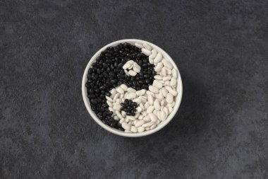 Karanlık bir arka planda Legumes. Gri tabakta beyaz fasulye ve siyah fasulye. Yin Yang imzala. Yatay konum. Üst görünüm.