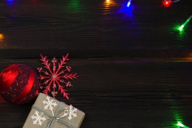 Noel hediyesi kutusu, kırmızı Noel topları ve yukarıdan koyu ahşap arka planda altın kar taneleri. Çok renkli çelenkler. Kış yeni yıl teması. Boşluğu kopyala