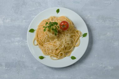 Geleneksel İtalyan spagettisi beyaz yuvarlak tabakta, arka planda. Makarna için malzemeler - kirazlı domates, parmesan, sarımsak, zeytinyağı, fesleğen. Üst görünüm.