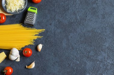 Makarna malzemeleri. Vişneli domates, spagetti makarna, sarımsak, fesleğen, parmesan ve baharatlar koyu grunge arka planda, fotokopi alanı, üst manzara. Yatay konum.