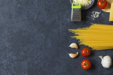 Yemek çerçevesi. Makarna malzemeleri. Vişneli domates, spagetti makarna, sarımsak, fesleğen, parmesan ve baharatlar koyu grunge arka planda, fotokopi alanı, üst manzara. Yatay konum.
