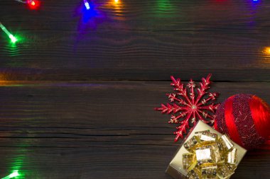 Noel hediyesi kutusu, kırmızı Noel topları ve yukarıdan koyu ahşap arka planda altın kar taneleri. Çok renkli çelenkler. Kış yeni yıl teması. Boşluğu kopyala