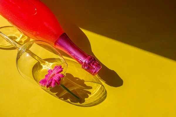 Festive party concept. Hard light hard shadows. Glass and bottle of pink champagne on a yellow background. Sunlight reveals the solid forms of glass and bottle shadows. Flat lay.