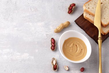 Beyaz kâse, doğal fıstık ezmesi, altın bıçak, fıstık ve hafif arka planda kızarmış ekmek. Vejetaryen geleneksel kahvaltısı yakın plan. Boşluğu kopyala