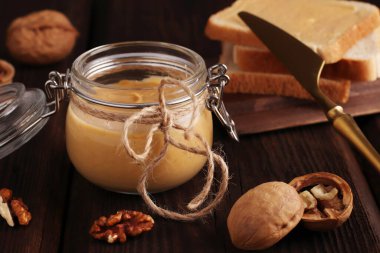 Vejetaryen geleneksel kahvaltı. Cam kavanozda doğal fıstık ezmesi, altın bir bıçak, ceviz ve tostlu sandviç, ahşap kahverengi arka planda. Vejetaryen geleneksel kahvaltı. Kapat..