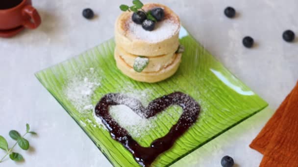 Mit Puderzucker garnieren japanische Pfannkuchen mit Blaubeeren auf einem quadratischen grünen Teller. Heller Hintergrund. Marmeladenherz. Leckeres Frühstück. — Stockvideo