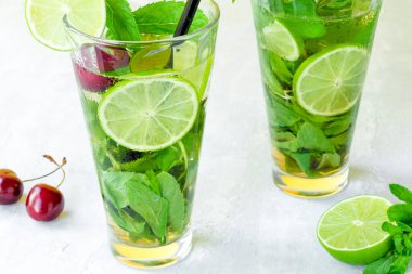 İki cam bardakta alkolsüz soğuk mojito. Limonata, limon ve nane arkaplanda. Kiraz oymacılığı.