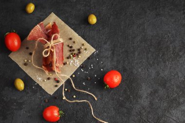 Organik ev yapımı yemekler. Parşömen kağıdının üzerine sicimle bağlanmış baharatlı kurutulmuş et parçaları. Baharatlar ve kaba tuz, kırmızı kiraz domatesleri, zeytinler. Boşluğu kopyala.