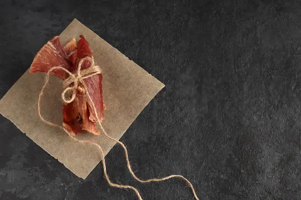 Egészséges Fűszeres Szárított Szárított Hús Fonallal Pergamenpapírra Kötve Sötét Háttérrel — Stock Fotó