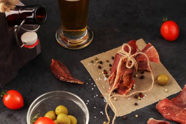 Bira için doğal atıştırmalık. Parşömen kağıdının üzerine sicimle bağlanmış baharatlı kurutulmuş et parçaları. Baharatlar, kaba tuz, kırmızı kiraz domatesleri, zeytinler. Organik ev yapımı yemekler..