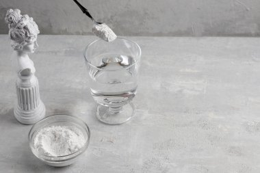 Cam bardakta hidrolize kolajen ve gri zemin üzerinde bir bardak su olan siyah bir kaşık. Sağlık ve güzellik için doğal destek. Boşluğu kopyala.