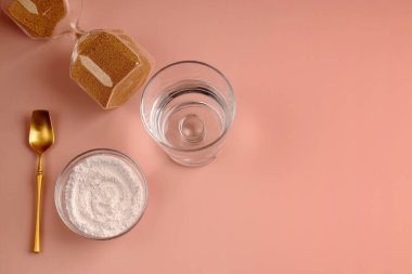 Yenilenme için doğal hidrolize kozmetik kolajen takviyesi. Altın kum saati ve toz kaşığı. Pembe arka planda sağlıklı ve yaşlanma karşıtı rahatlama kavramı. Yukarıdan bak. Boşluğu kopyala.