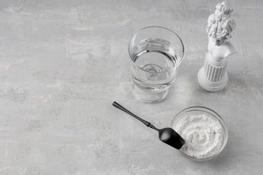 Cam bardakta kolajen ve beton zeminde bir bardak suyla siyah kaşık. Hidrolize edilmiş sağlık ve güzellik için doğal destek. Boşluğu kopyala.