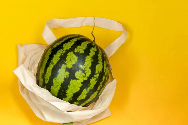 Watermelon in eco packaging on a yellow background. Detox in a reusable shopping bag. Zero waste healthy food delivery concept. Copy space.