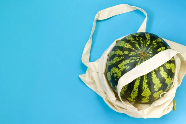Watermelon in eco packaging on a blue background. Detox in a reusable shopping bag. Zero waste healthy food delivery concept. Copy space.