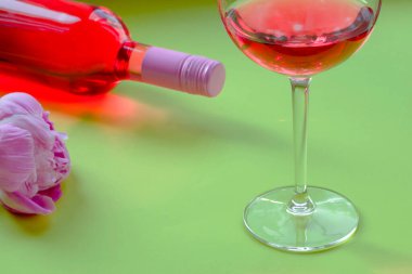 Romantik akşam yemeği ya da kahvaltı. Büyük bardakta gül şarabı ve yeşil arka planda güzel şakayıklar olan yaratıcı yaz kompozisyonu. Kutlama konsepti