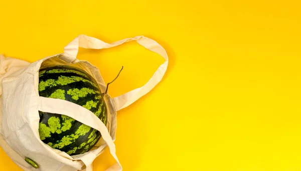Detox in a reusable shopping bag. Watermelon in eco packaging on a yellow background. Zero waste healthy food delivery concept. Copy space.