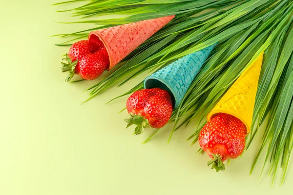 Summer creative concept. Colored waffle cones for ice cream with fresh strawberries on a light background. Copy space.