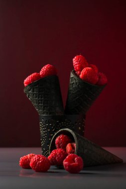 Koyu arkaplanda dondurma için waffle külahlı doğal taze ahududu. Alçakgönüllülük. Vejetaryenlik için yaz hasadı. Dikey konum