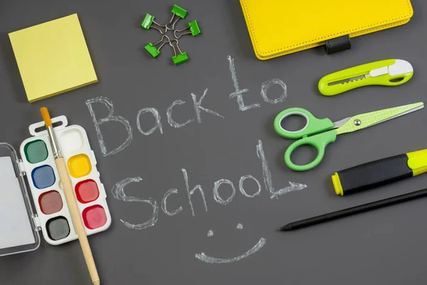 Back to school concept with chalk inscription. Bright office and school supplies on a dark background. Social distance. Stay safe