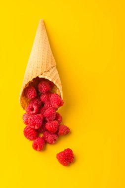 Minimalizm. Sarı masadaki waffle külahında ahududu patlaması. Yukarıdan bak. Sağlıklı gıda konsepti. Dikey konum