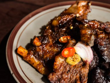 Endonezya usulü ızgara kaburga İga Bakar yanında tatlı soya jölesi ve taze biber sosu, Geleneksel Biftek Kaburgası Seramik Tabak ve Rustik Tahta Masa Arkaplanı, Asya Gastronomi Manzarası