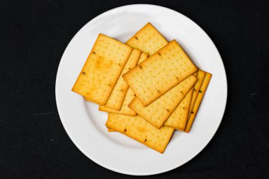 Beyaz Tabakta Tohumlu Çıtır Altın Krakerler, Fırın ve Mutfak Arkaplanı İçin Dikdörtgen Buğday Bisküvileri Üst Manzarası, Siyah Masa Üzerinde Savory Çıtırtılı Atıştırmalıklar