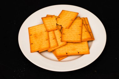 Beyaz tabakta tohumlu çıtır altın buğday krakerleri, Fırın ve Mutfak Markası Bisküvileri Üst Manzarası, Minimalist Siyah Masa Arkaplan Yatağında Sağlıklı Çıtır Atıştırmalık