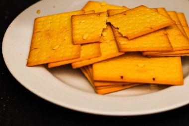 Beyaz tabakta tohumlu çıtır altın buğday krakerleri, Fırın ve Mutfak Markası için dikdörtgen bisküvilerin üst görüntüsü, Minimalist Siyah Masa Düz Yatağında Sağlıklı Çıtır Atıştırmalıklar