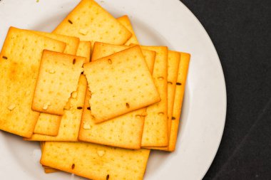 Kırık ve Tam Altın Buğdaylı Krakerler, Beyaz Tabakta Tohumlar, Fırın ve Mutfak Markası Bisküvileri Üst Görüş, Minimalist Kara Arkaplan Üzerine Açık Çıtır Atıştırmalık