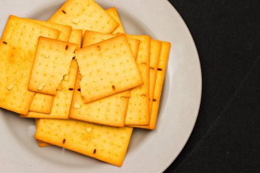 Beyaz Tabakta Tohumlu Çıtır Buğday Krakerleri, Fırın ve Mutfak Arkaplanı İçin Altın Kahverengi Dikdörtgen Bisküvileri Üst Görünümü, Minimalist Siyah Masa Düz Yatağı Sağlıklı Taze Atıştırmalık
