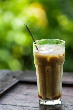 Ahşap Masada Metal Kaşıklı Buzlu Kahve Latte, Güzel Mezuniyetli Soğuk Süt Kahve ve Gastronomi ve Cafe Yaşam Tarzı İçin Doğal Yeşil Bokeh Arkaplanı